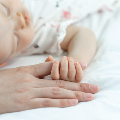 The newborn baby sleeps and grabs the mother's finger