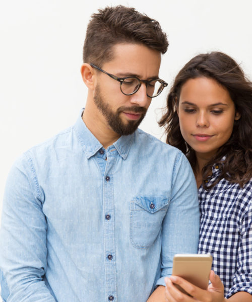 Focused couple reading message on cellphone screen. Young woman in casual and man in glasses in glasses posing isolated over white background. Mobile phone using concept